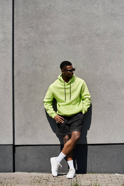 Handsome African American man in lime hoodie leaning against wall. - Photo, Image