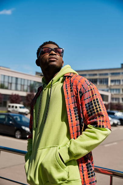 Handsome African American man in green hoodie and sunglasses balancing on railing. - Photo, Image