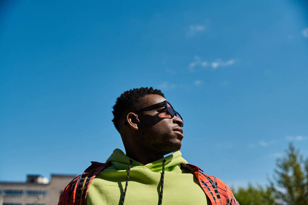 Schöner afroamerikanischer Mann in grünem Kapuzenpulli blickt in den Himmel. - Foto, Bild