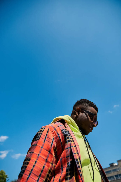 Fešák Afroameričan v módní kostkované bundě stojící pod jasnou modrou oblohou. - Fotografie, Obrázek