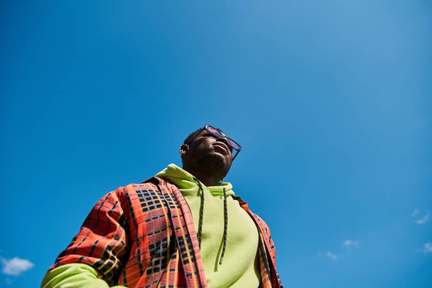 Όμορφος Αφροαμερικανός με κομψό σακάκι κοιτάζει ψηλά στον ουρανό.. - Φωτογραφία, εικόνα