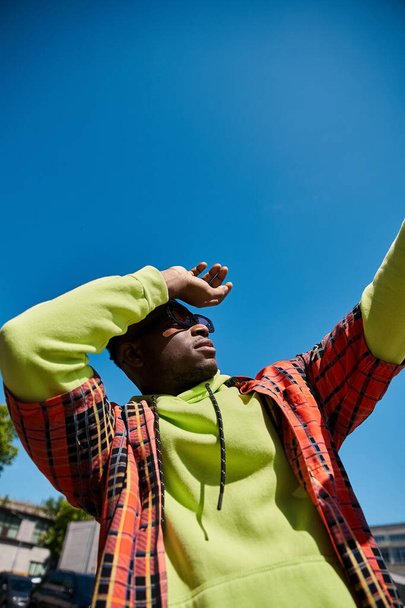 Afrikkalainen amerikkalainen mies vihreässä takissa pitää kädestä taivaaseen. - Valokuva, kuva