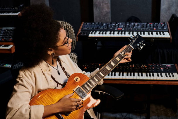 Талантливая женщина, играющая на гитаре со страстью в профессиональной студии звукозаписи для репетиции музыкальной группы. - Фото, изображение