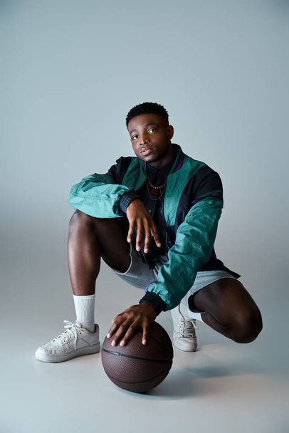 Young African American man in stylish attire crouching with a basketball ball. - Photo, Image