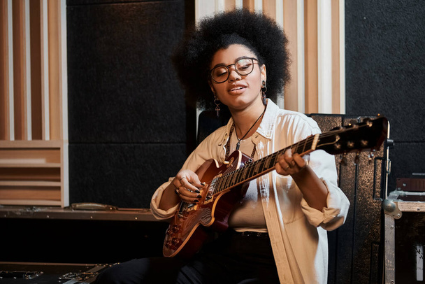 Μια γυναίκα με γυαλιά που παίζει κιθάρα με πάθος σε στούντιο ηχογράφησης κατά τη διάρκεια πρόβας μουσικής μπάντας.. - Φωτογραφία, εικόνα