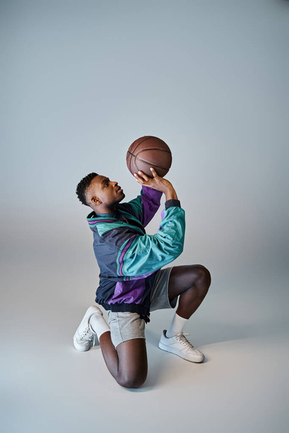Ένας κομψός Αφροαμερικάνος μπασκετμπολίστας σκύβει για να πιάσει μια μπάλα. - Φωτογραφία, εικόνα