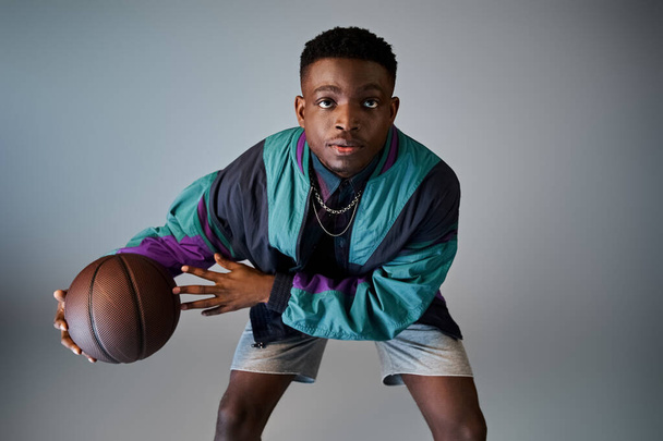 灰色の背景に対してバスケットボールを保持するスタイリッシュな若いアフリカ系アメリカ人男性. - 写真・画像