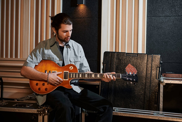 Un hombre toca apasionadamente una guitarra en medio de un equipo de música en un estudio de grabación durante un ensayo de la banda de música. - Foto, imagen