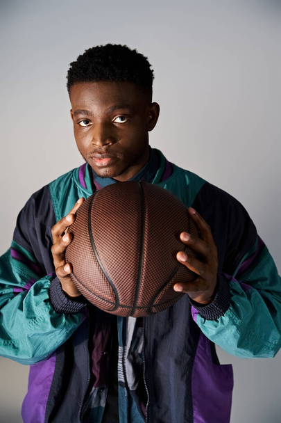 Handsome African American man in fashionable attire holding basketball on white background. - Photo, Image
