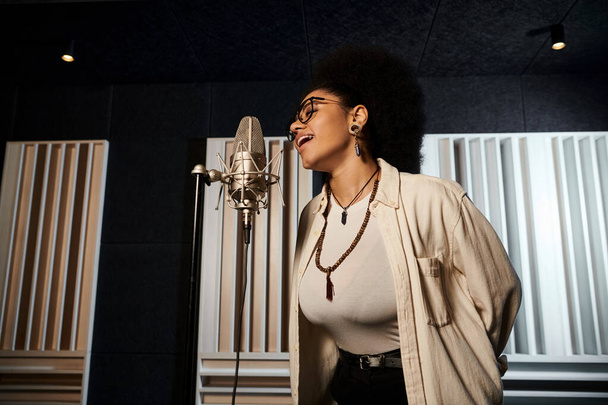 Nainen laulaa intohimoisesti mikrofoniin levytysstudiossa musiikkibändin harjoitusten aikana.. - Valokuva, kuva