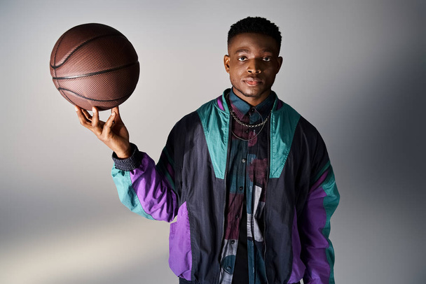 グレーの背景に対してバスケットボールを保持するファッショナブルなアフリカ系アメリカ人男性. - 写真・画像