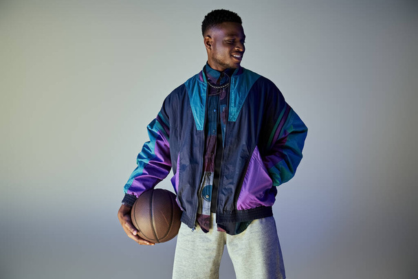 Fiatal afro-amerikai férfi elegáns öltözékben, kezében egy kosárlabda. - Fotó, kép