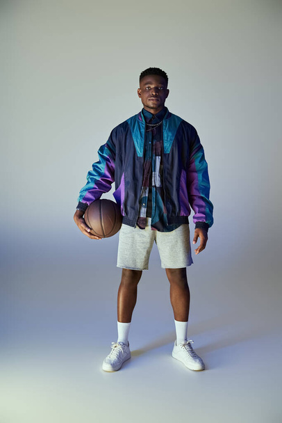 白い背景の前にバスケットボールを持っているファッショナブルな若いアフリカ系アメリカ人男性. - 写真・画像