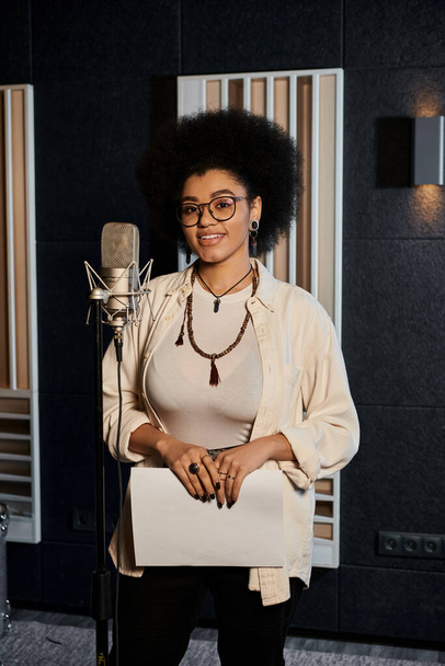 A talented woman stands poised in front of a microphone, ready to lend her voice to a music band rehearsal in a recording studio. - Photo, Image