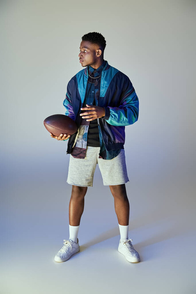 白い背景に対してサッカーを保持するファッショナブルな服装のアフリカ系アメリカ人男性. - 写真・画像