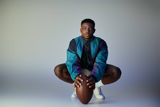 Un homme afro-américain élégant et athlétique accroupi avec un ballon de football. - Photo, image