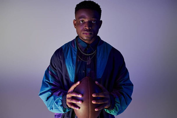 Schöner afroamerikanischer Mann in der Hand eines Fußballs vor einem leuchtend blauen Hintergrund. - Foto, Bild