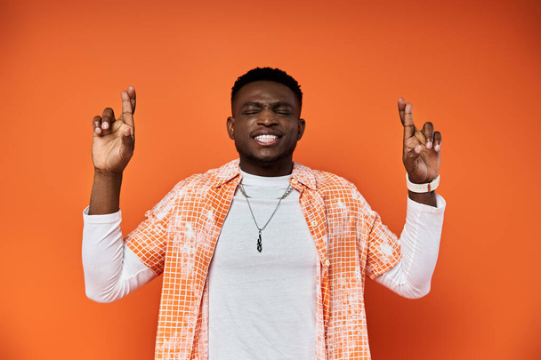 Ein modischer junger Afroamerikaner in orangefarbenem Hemd macht mit seinen Händen eine Geste. - Foto, Bild