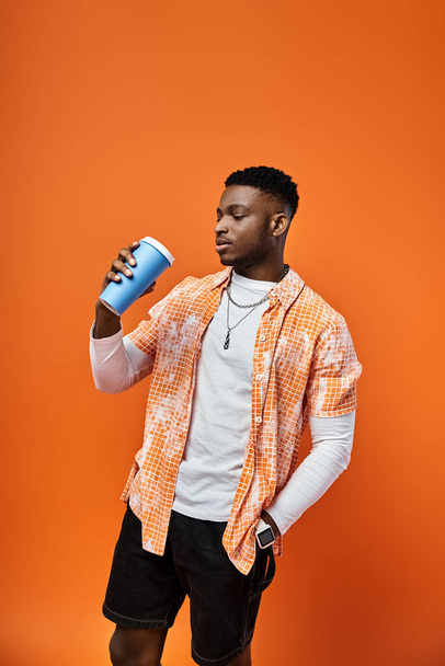 African American man in fashionable attire holding cup against bright orange background. - Photo, Image