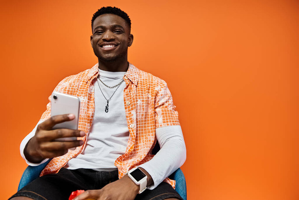 Handsome African American man in stylish attire sitting in a chair while using a cell phone. - Photo, Image