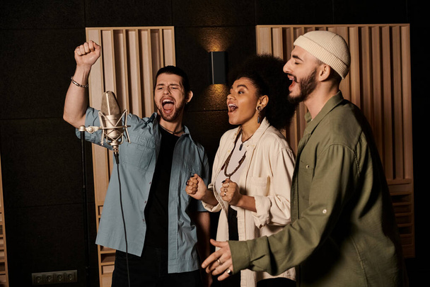 Tři jednotlivci vášnivě zpívají do mikrofonu v nahrávacím studiu během zkoušky hudební kapely. - Fotografie, Obrázek
