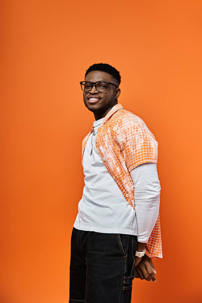 Uomo afroamericano in camicia arancione alla moda colpisce una posa contro uno sfondo corrispondente. - Foto, immagini
