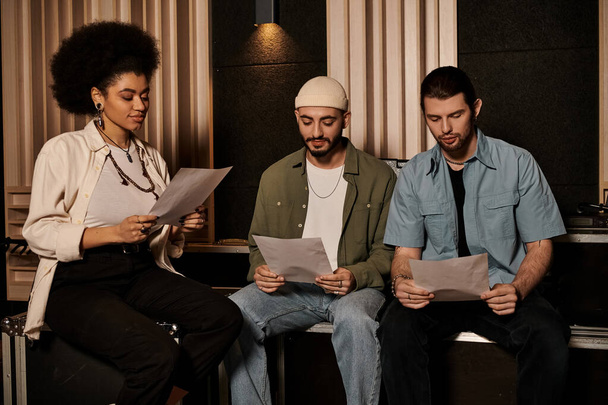 Tři lidé v nahrávacím studiu, sedí, soustředí se, čtou noviny pro zkoušku hudební kapely. - Fotografie, Obrázek