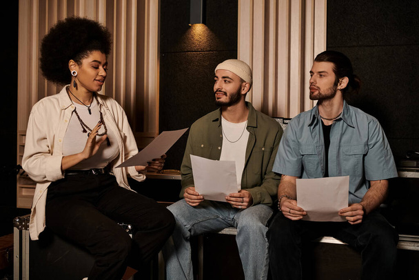 Tři hudebníci sedí v nahrávacím studiu, drží hudební listy a diskutují o své další písni. - Fotografie, Obrázek