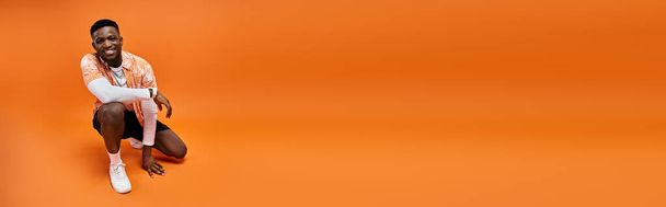 活気に満ちたオレンジ色の背景でクロージングスタイリッシュな服装のファッショナブルなアフリカ系アメリカ人男性. - 写真・画像