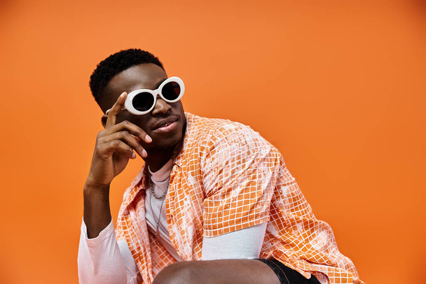 Афроамериканец в солнечных очках сидит на оранжевом фоне. - Фото, изображение