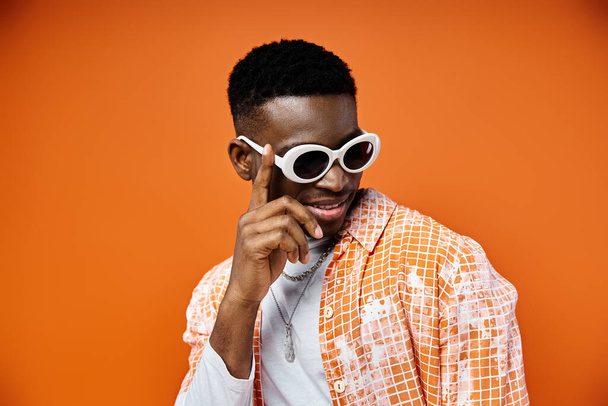Handsome African American man in sunglasses poses stylishly on orange background. - Photo, Image
