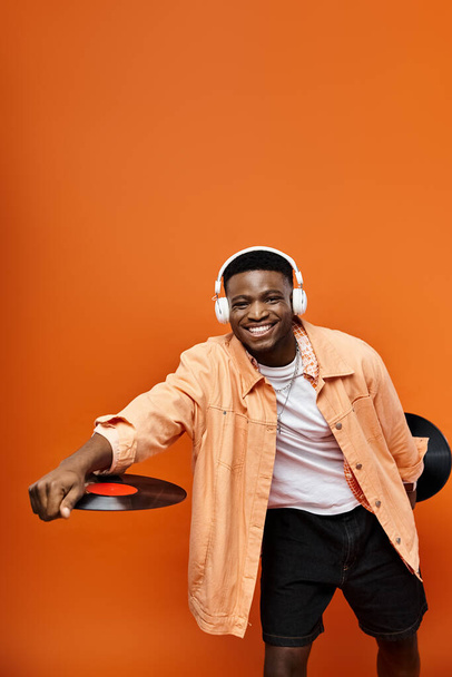 Knappe Afro-Amerikaanse man in stijlvolle kleding met een record op een oranje achtergrond. - Foto, afbeelding