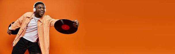Fashionable African American man in stylish attire holding a vinyl record against a bright orange backdrop. - Photo, Image