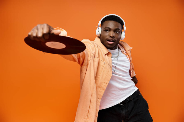Homem preto elegante com fones de ouvido segurando um recorde no fundo laranja. - Foto, Imagem