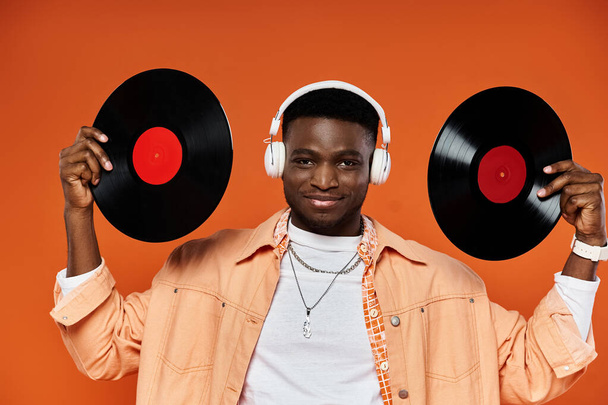 Schöner schwarzer Mann mit Schallplatten vor orangefarbenem Hintergrund. - Foto, Bild