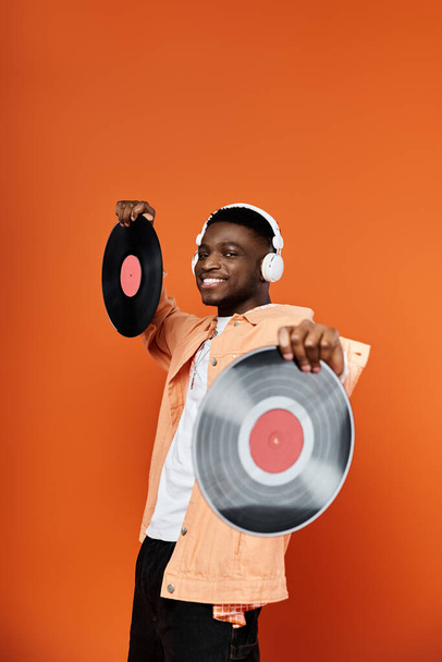 オレンジ色の背景にビニールレコードを持っているスタイリッシュな若いアフリカ系アメリカ人男性. - 写真・画像