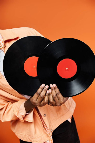 Hombre afroamericano guapo sosteniendo dos discos de vinilo sobre un fondo naranja. - Foto, imagen
