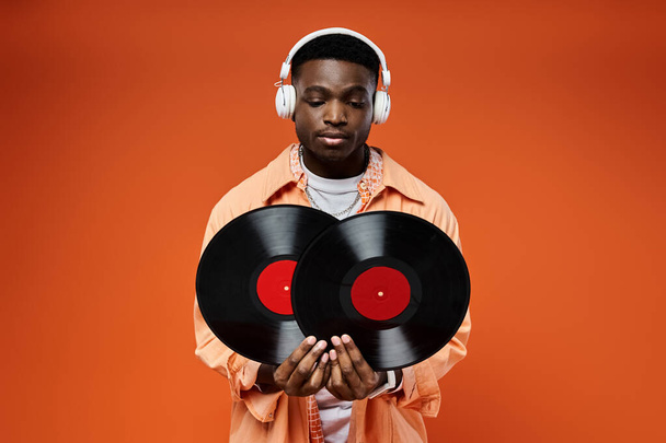 Όμορφος Αφροαμερικανός με στυλάτη ενδυμασία κρατώντας ένα δίσκο και ακούγοντας με ακουστικά. - Φωτογραφία, εικόνα