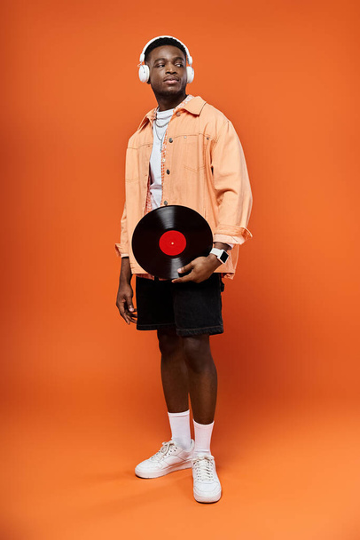 Fashionable African American man holding a vinyl record on an orange background. - Photo, Image
