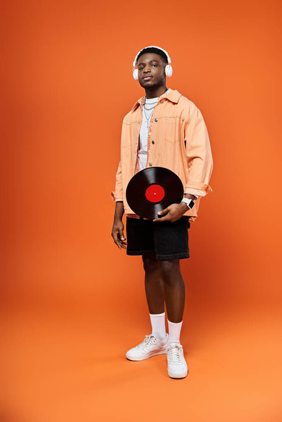 Fashionable African American man holds record on bright orange backdrop. - Photo, Image