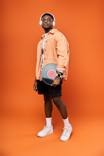 Stilvoller Mann mit Kopfhörer, der eine Platte auf orangefarbenem Hintergrund hält. - Foto, Bild
