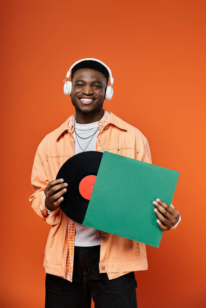Fešák Afroameričan ve stylovém oblečení, drží vinylovou desku se sluchátky. - Fotografie, Obrázek