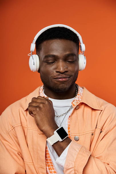 Κομψό Αφρο-Αμερικανός άνθρωπος σε ακουστικά με φόντο ζωντανό πορτοκαλί. - Φωτογραφία, εικόνα