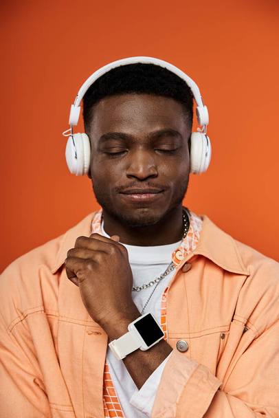 明るいオレンジ色の背景に対してヘッドフォンでスタイリッシュなアフリカ系アメリカ人男性. - 写真・画像