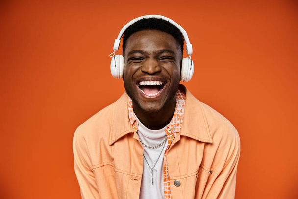 Homem negro elegante sorri usando fones de ouvido no fundo laranja. - Foto, Imagem