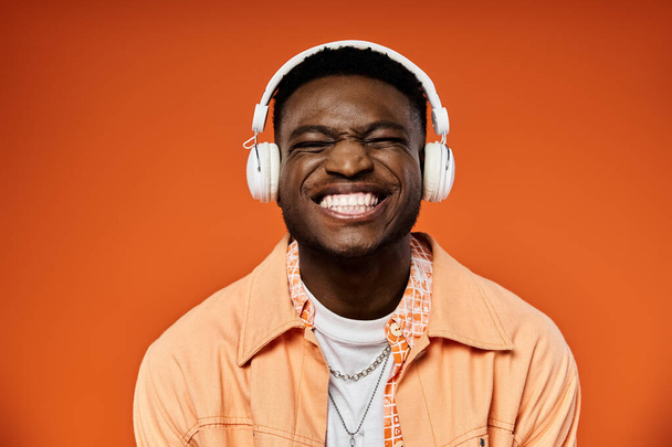 Homem afro-americano elegante com fones de ouvido sorri contra pano de fundo laranja. - Foto, Imagem