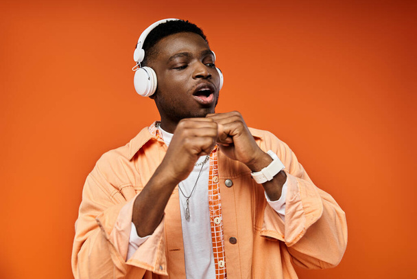 Ένας μοντέρνος νεαρός Αφροαμερικανός που φοράει ακουστικά σε πορτοκαλί φόντο.. - Φωτογραφία, εικόνα