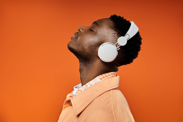 Stylish young man with headphones gazes at orange background. - Photo, Image