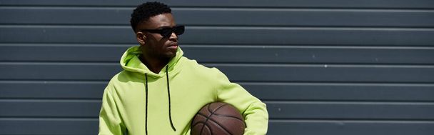 Handsome African American man in green hoodie holds basketball. - Photo, Image