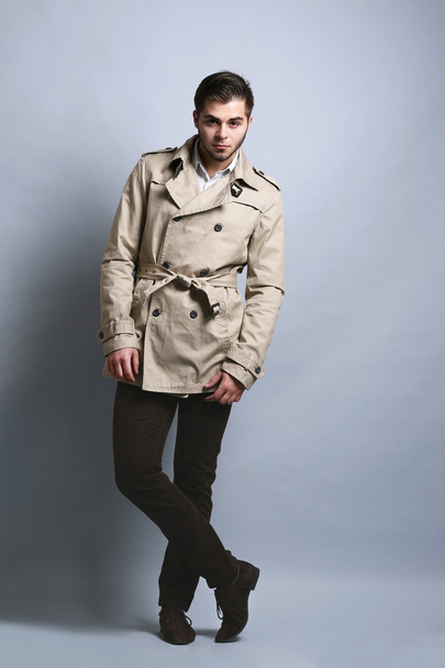 Young man in coat on gray background - Фото, изображение